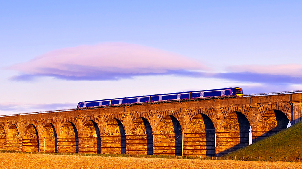 Old masonry arched viaduct carrying a train near Edinburgh, Scotland with sunset lighting